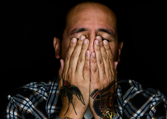 Man with tattoos covering his face with hands, illustrating moments men share that would be outrageous if genders reversed.