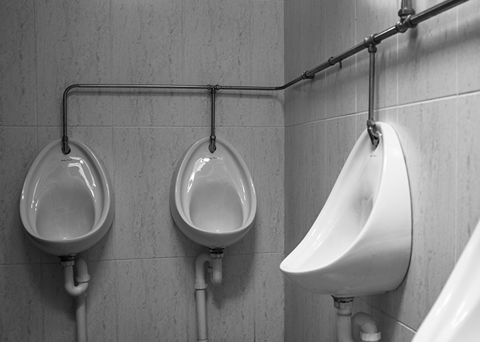 Three white urinals mounted on tiled restroom walls with visible plumbing, illustrating moments from men's experiences.