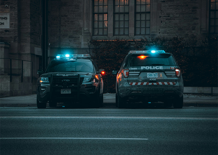 Two police vehicles with flashing lights parked on a city street at dusk, highlighting moments that challenge gender norms.