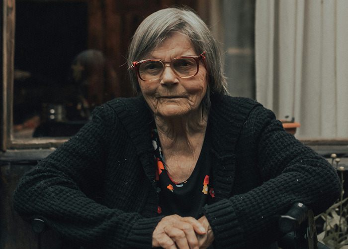 Elderly woman with glasses wearing a black cardigan, reflecting on moments that would be outrageous if genders reversed.