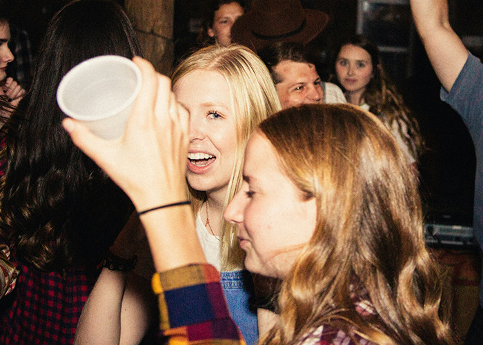 Group of people socializing at a lively party with men and women sharing outrageous moments from reversed gender experiences.