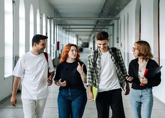 Four young men and women walking and talking in a hallway, illustrating moments men share that differ by gender.