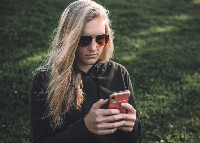 Woman wearing sunglasses outdoors, focused on her phone, illustrating moments that would be outrageous if genders were reversed