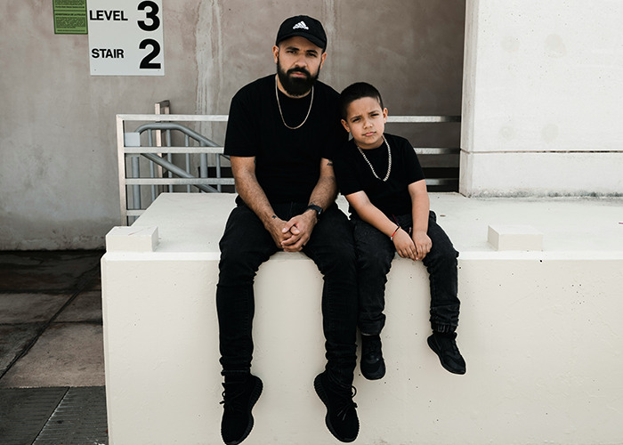 Man and boy sitting on a ledge wearing black clothes, illustrating moments shared by men in everyday life.