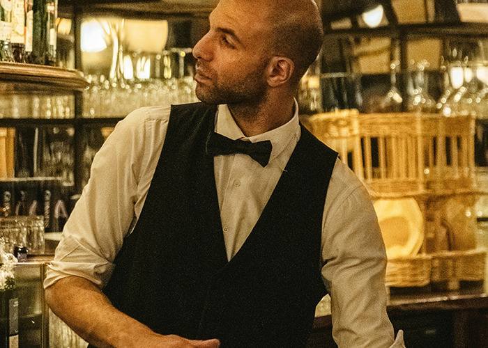Man in a black vest and bow tie working as a bartender, highlighting moments that would be outrageous if genders reversed