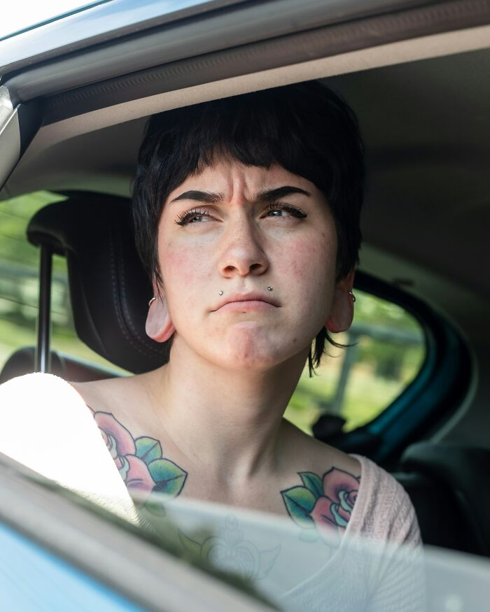 Young woman with tattoos looking annoyed inside a car, illustrating a turn off men want women to know.