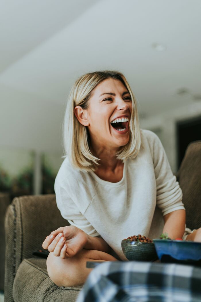 Woman laughing joyfully on a couch, illustrating body language that relates to things men want women to know are a turn off.
