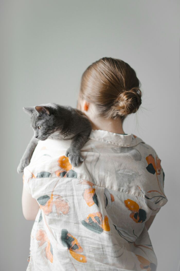 Woman with a messy bun holding a gray cat on her shoulder, illustrating things men find a turn off in women.