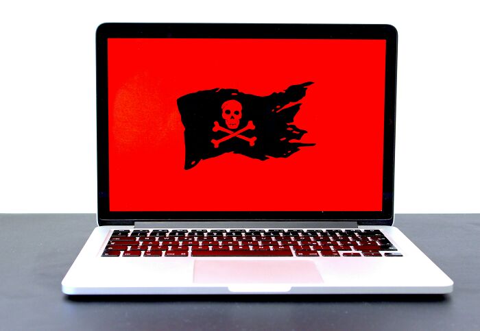 Laptop screen displaying a tattered pirate flag with skull and crossbones symbol representing online piracy risks.
