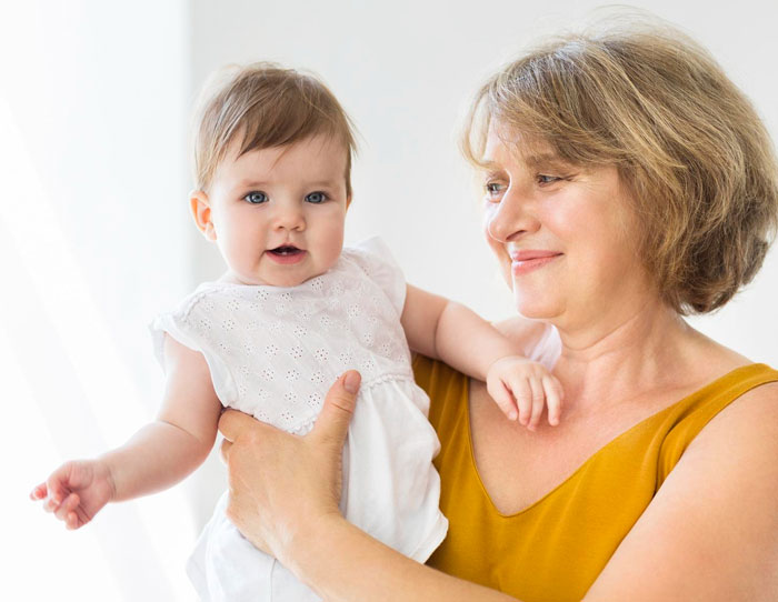 Woman in a mustard top holding a baby girl in white dress smiling, representing mil calls herself mommy theme