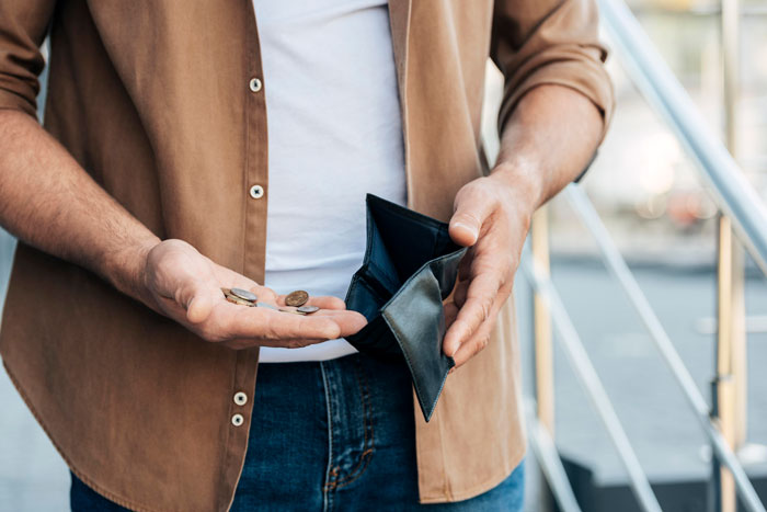Man holding empty wallet and few coins, symbolizing financial stress related to paying for fancy restaurant dinner.