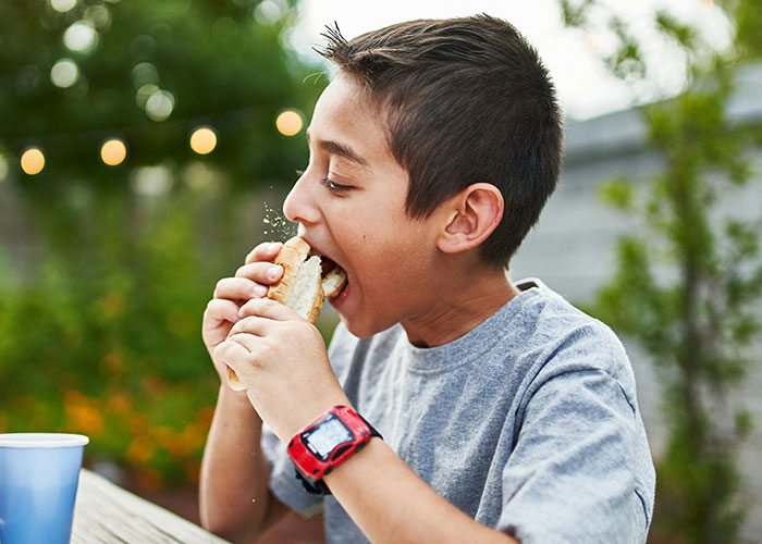 Boy wearing a red watch eating fast food outdoors, highlighting concerns about kids being fed unhealthy meals by MIL.