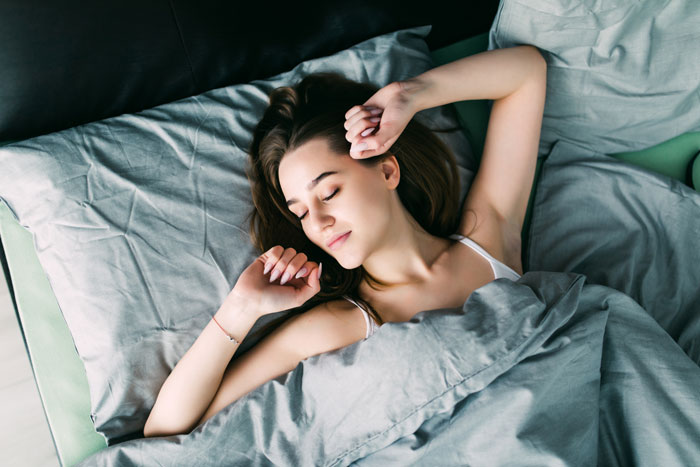 Young woman sleeping peacefully in bed under gray blankets in a calm bedroom setting at night. Young woman sleeping peacefully in bed under gray blankets in a calm bedroom setting at night.