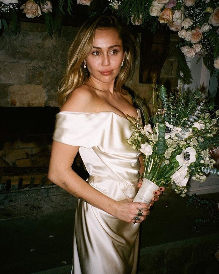 Miley Cyrus in an off-shoulder wedding dress holding a bouquet, amid fans calling out Demi Lovato for wedding dress controversy.