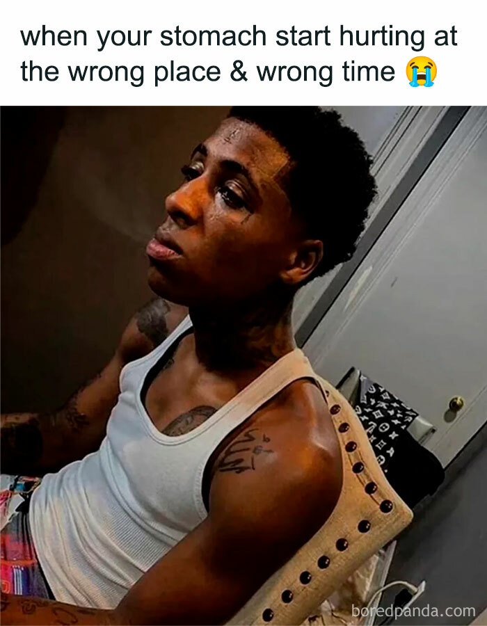 Young man in a white tank top looking pained, paired with a mocking posts jokes memes caption about stomach pain timing.