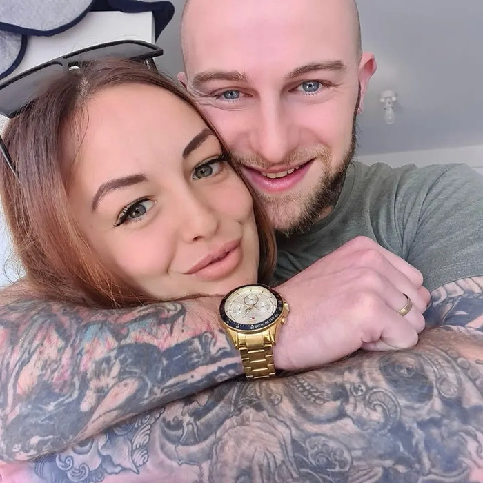Young couple embracing and smiling, with detailed tattoos and a gold watch visible, related to heart missing autopsy case.