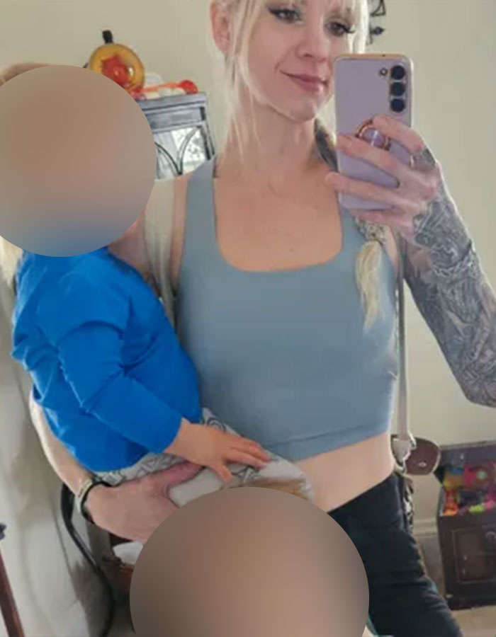 Woman with tattoos taking a mirror selfie holding a young child in a blue shirt, related to racist playground incident raising funds.