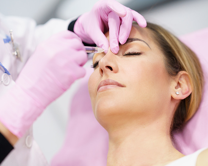 Woman receiving cosmetic injection near eyes from gloved medical professional in a clinical setting, highlighting mom wakes from surgery story.