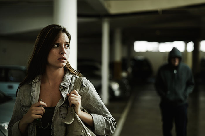 Woman looking worried while walking in a dark parking garage with a hooded figure approaching, highlighting instinct and caution.