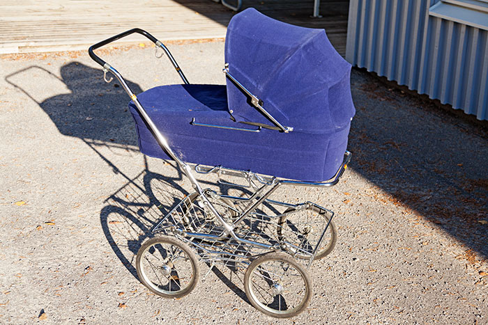 Vintage baby stroller with a blue fabric cover on a sunlit urban sidewalk, evoking real-life instinct stories.