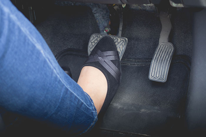 Person wearing black flats and blue jeans pressing the gas pedal in a car, symbolizing instinct in real-life stories.