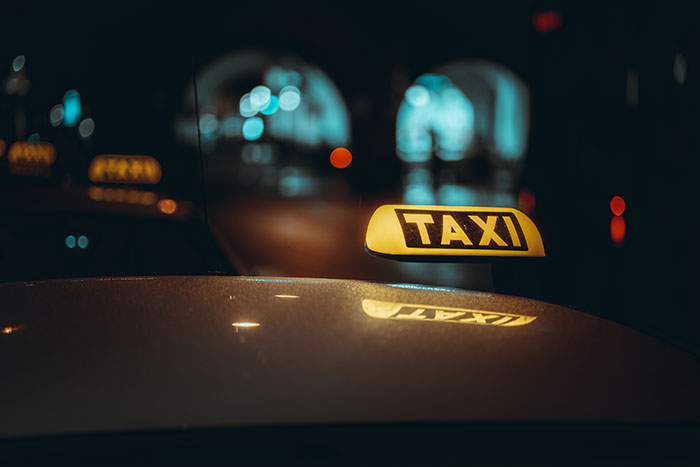 Taxi sign illuminated at night with blurred city lights in the background, reflecting instinct and safety during late night strolls.