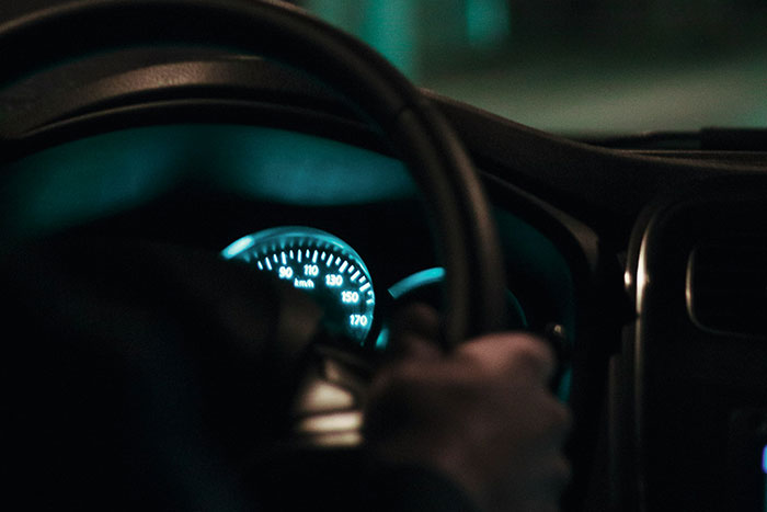Person gripping steering wheel at night inside car, capturing a moment where instinct is everything during late night drives.