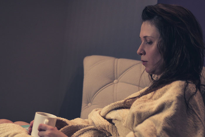 Woman in a bathrobe holding a cup, deep in thought, illustrating instinct and real-life stories of caution and intuition.