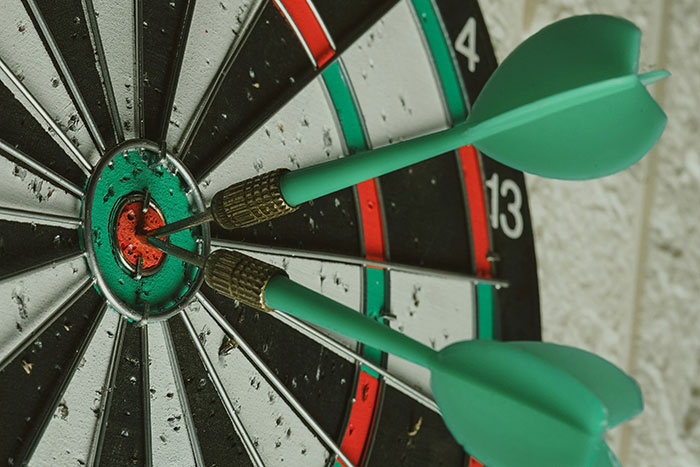 Close-up of a dartboard showing three green darts hitting the bullseye, symbolizing instinct and precision.