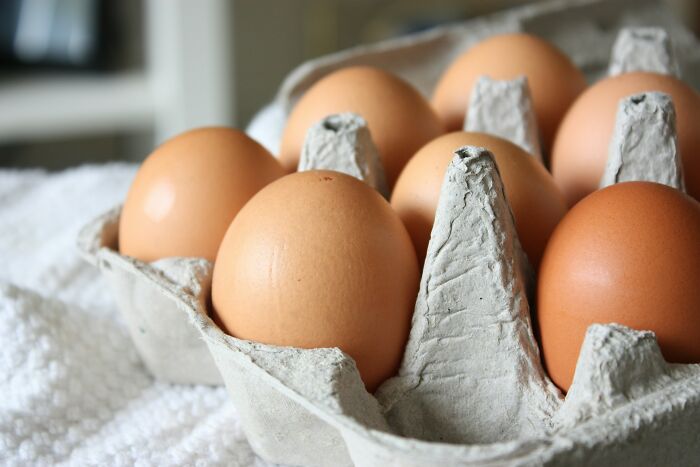 Brown eggs in a cardboard carton on a white cloth, illustrating common foods that go bad more quickly.