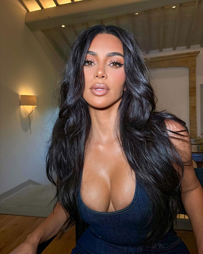 Kim Kardashian with long dark hair and makeup posing indoors, exploring the science behind the most beautiful woman in the world.