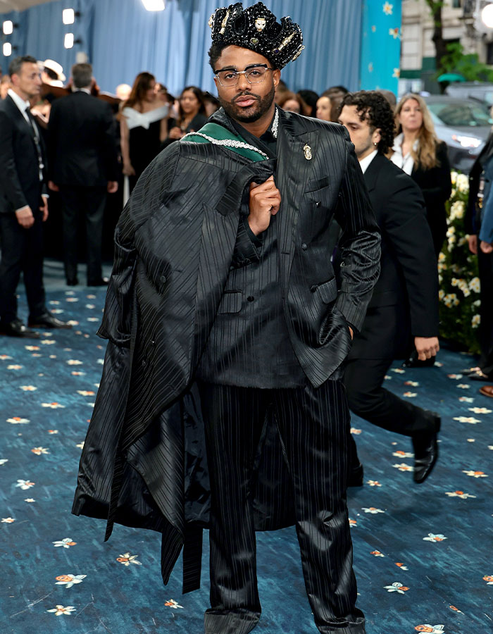 Man dressed in a black pinstripe suit and ornate crown posing on the red carpet at Met Gala 2025 fashion event.