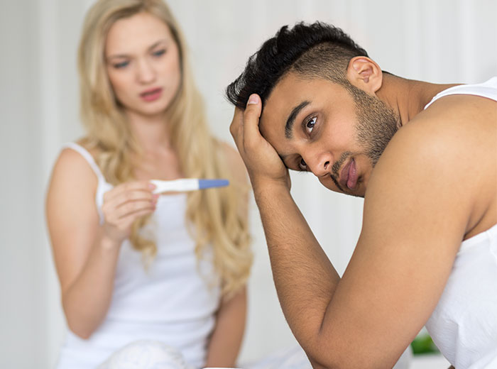 Man looks stressed while woman holds a positive pregnancy test, depicting challenges of raising a newborn alone.