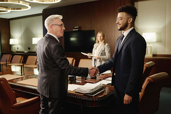Two men in suits shaking hands in a conference room while a woman observes in a professional setting about man raising newborn alone.