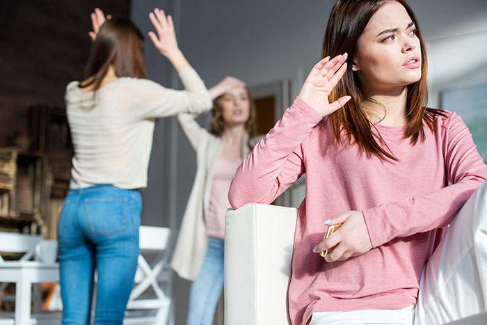 Woman in pink shirt looks upset while two daughters argue in background, illustrating family conflict involving half-brother.