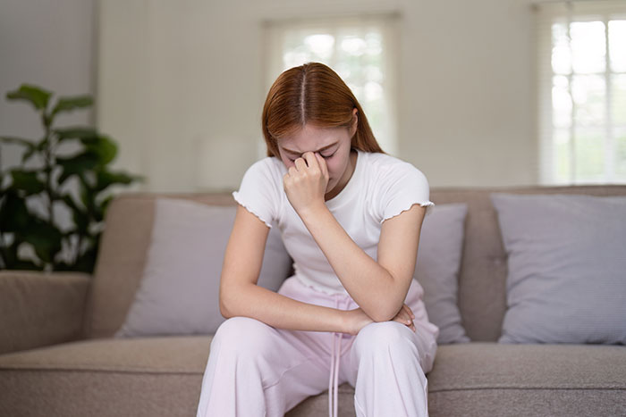 Teen girl looking upset and stressed sitting on a couch after mom blows up at daughters for half-brother issues.