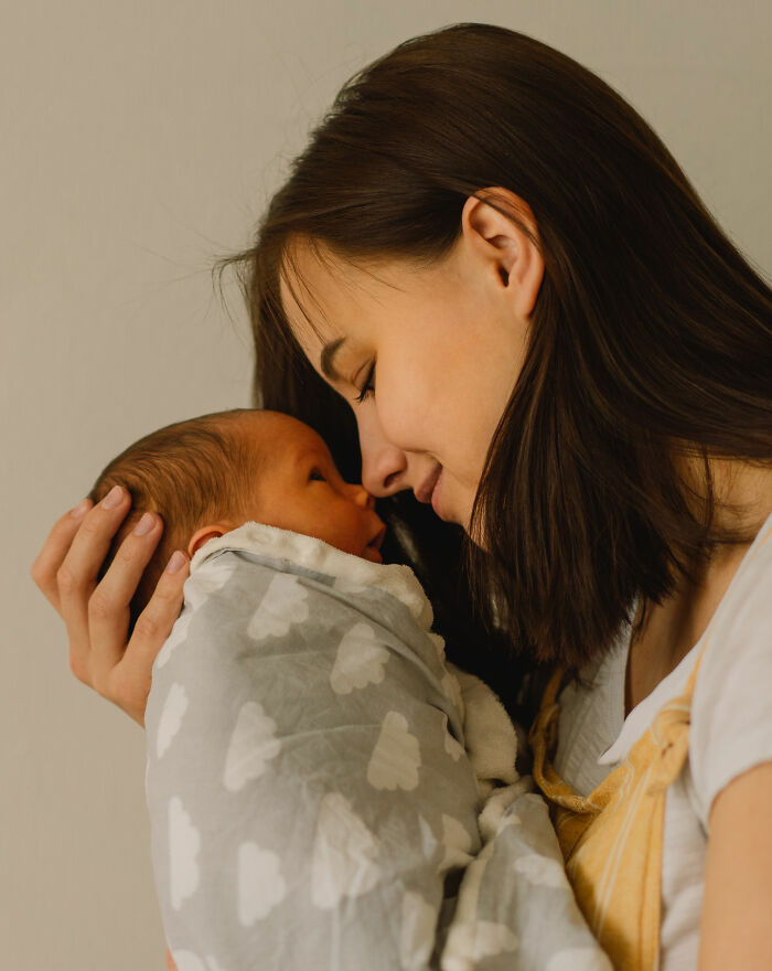 Mother tenderly holding her newborn wrapped in a cloud-patterned blanket, reflecting on hilariously bad names and parenting choices.