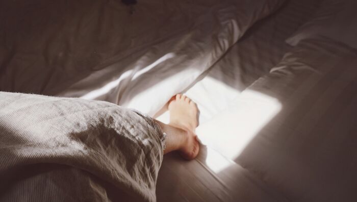 A person’s foot peeking from under a blanket on a bed, illustrating funny and weird girlfriend secret moments.