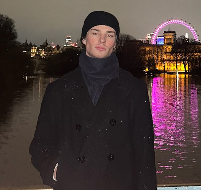 Young man wearing a black beanie and coat at night by a river, sparking massive thirst over guy in Lana Del Rey Met Gala photo.