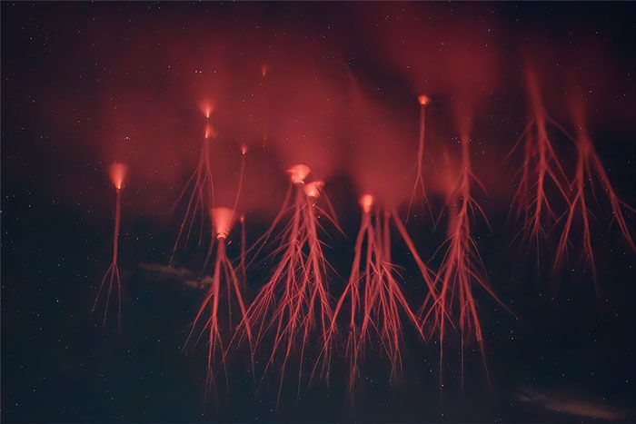 Rare natural phenomena showing red sprites glowing above a dark night sky filled with stars and scattered clouds.