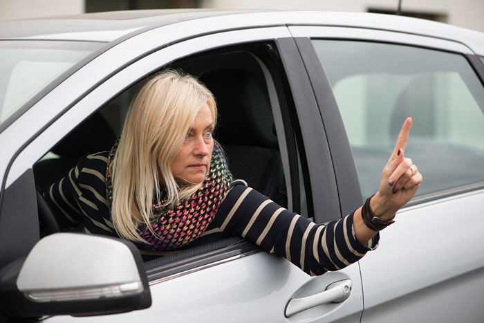 Woman in striped shirt sitting in car, pointing finger outside the window, showing entitlement and parking dispute with neighbor. Woman in striped shirt sitting in car, pointing finger outside the window, showing entitlement and parking dispute with neighbor.