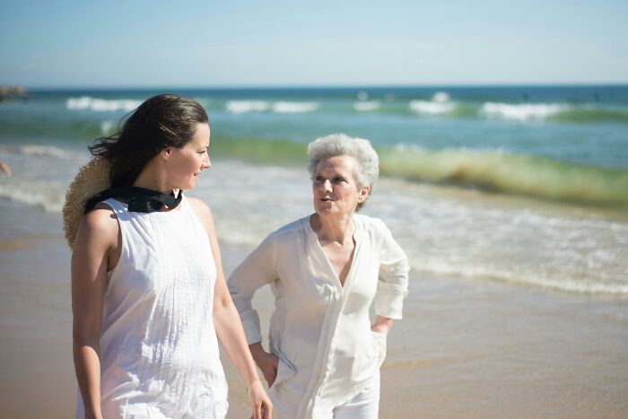 Daughter and grieving mom walking on beach, daughter supporting mom’s new romance despite red flags on first visit.