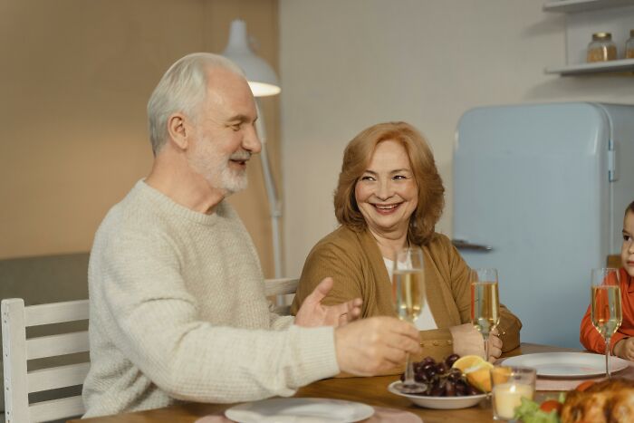 Elderly couple enjoying a drink at home as daughter watches, supporting grieving mom’s new romance and concerns.