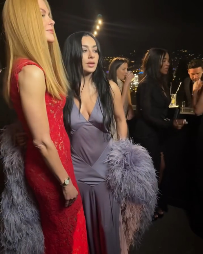 Nicole Kidman with natural hair in a red dress at a night event, surrounded by guests against a city skyline backdrop.