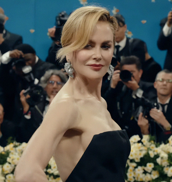 Nicole Kidman at Cannes red carpet, showing a wig topper exposed during a stylish appearance with photographers behind.