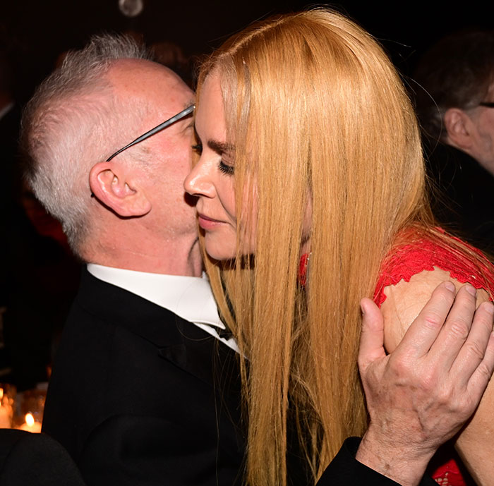 Nicole Kidman with long red hair in a red dress embraces a man in glasses and a black suit at a formal event.