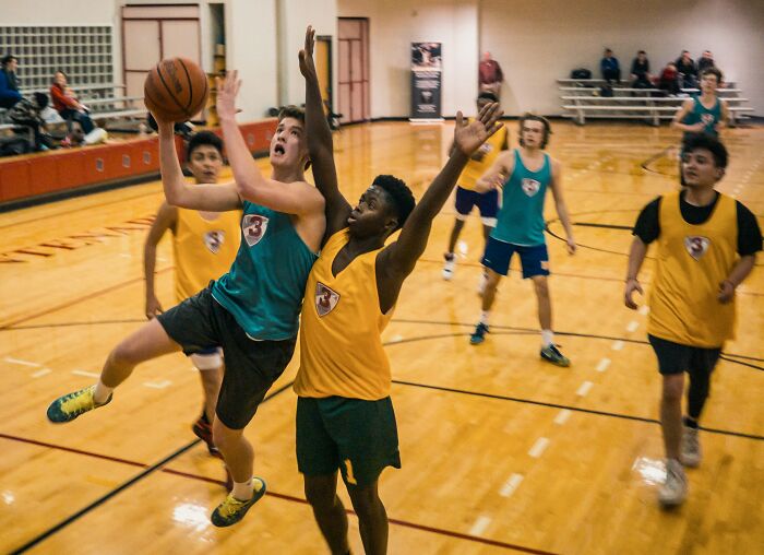 Teen basketball players competing in a gym during an intense game, illustrating mind-boggling beliefs smart people still hold.