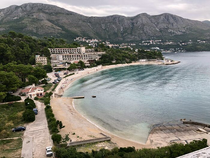Secluded beach and abandoned hotel in a faded tourist destination with mountains and calm sea in the background.