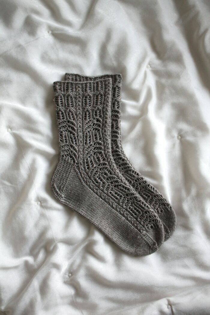 Pair of gray knitted socks on a white bedspread, illustrating mundane things that make people sick like wearing unclean clothing.