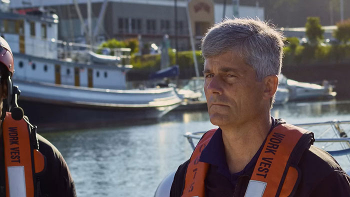 Man in a work vest standing by a marina with boats, reflecting the OceanGate CEO’s wife’s chilling reaction moment. Man in a work vest standing by a marina with boats, reflecting the OceanGate CEO’s wife’s chilling reaction moment.